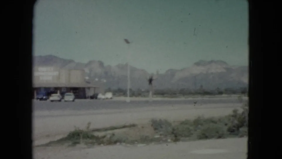 A large truck moves through the Nevada roadside scene, with utility poles, scrub and a mountain range visible beyond the road.