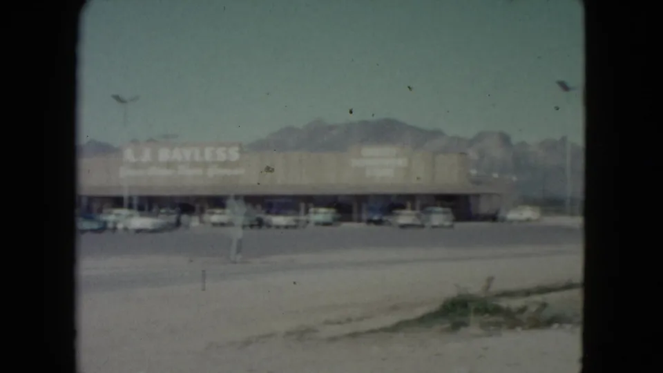 1960 Nevada frame with the A.J. Bayless sign visible on a long storefront beyond a wide parking lot.