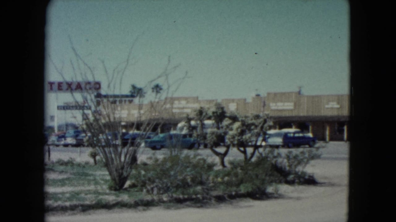 1960 Nevada town street with a visible Texaco sign, low commercial buildings, parked cars, and desert landscaping.
