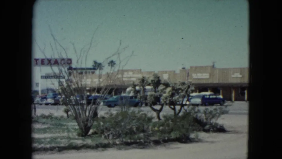 1960 Nevada town street with a visible Texaco sign, low commercial buildings, parked cars, and desert landscaping.