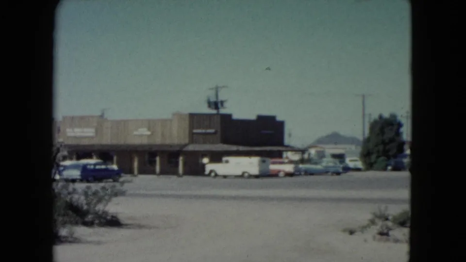 End of a 1960 Nevada roadside pass, showing storefronts, parked cars, utility poles, and a distant mountain beyond the street.