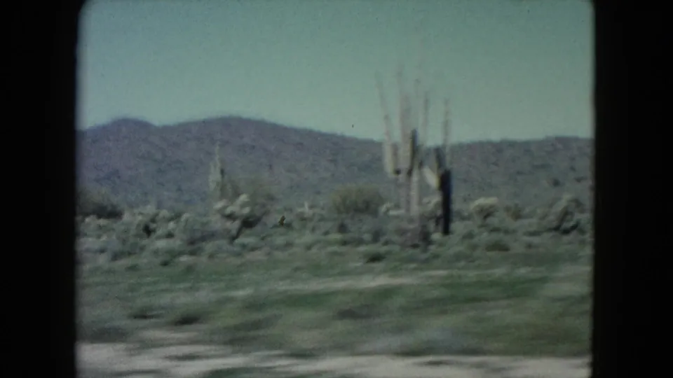 Moving Nevada desert view from 1960 home-movie footage, with blurred scrub, cactus-like plants, and mountains in the distance.