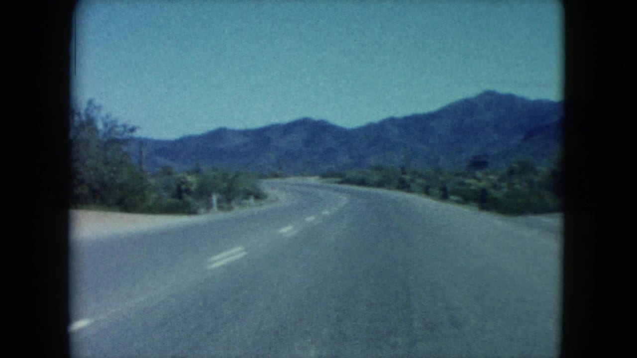 1960 Nevada 8mm view from a moving car on a quiet desert highway with shrubs and mountains ahead.