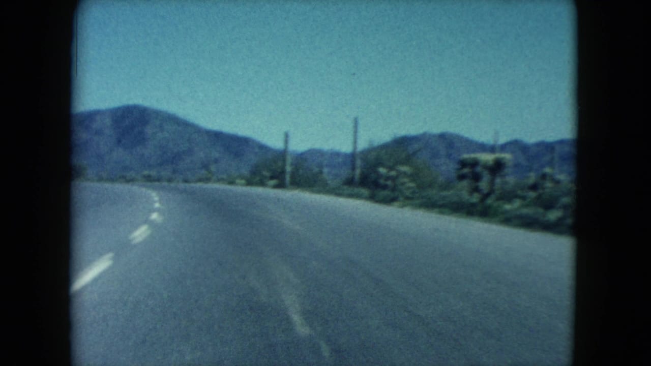 Paved desert highway curving toward distant mountains under a hazy sky.