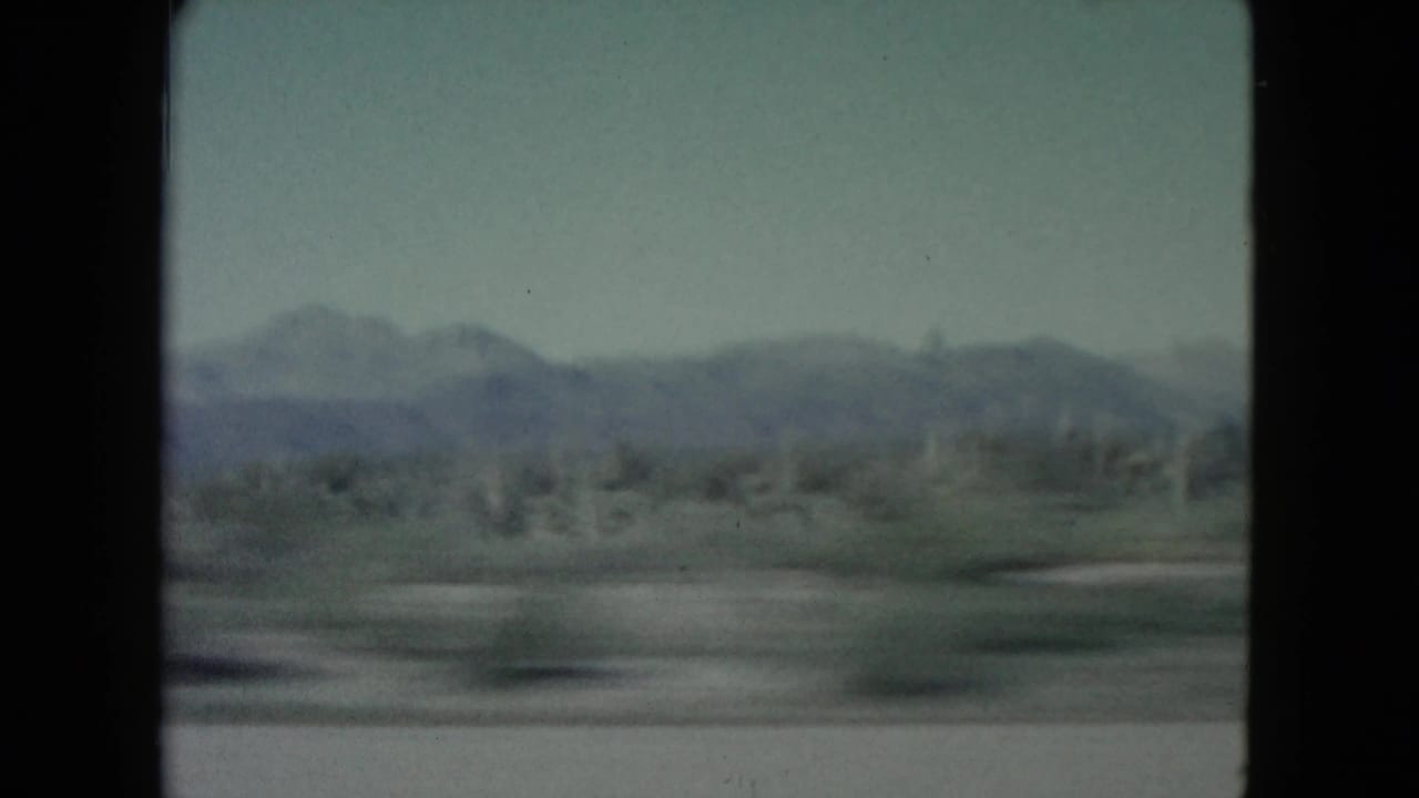 End frame of the 1960 Nevada road-trip clip, with soft mountains, roadside desert scrub, blue sky, and visible 8mm film texture.