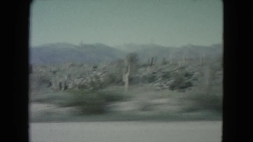 1960 Nevada desert terrain with cacti, brush, and low mountains filmed through soft motion blur from a moving car.