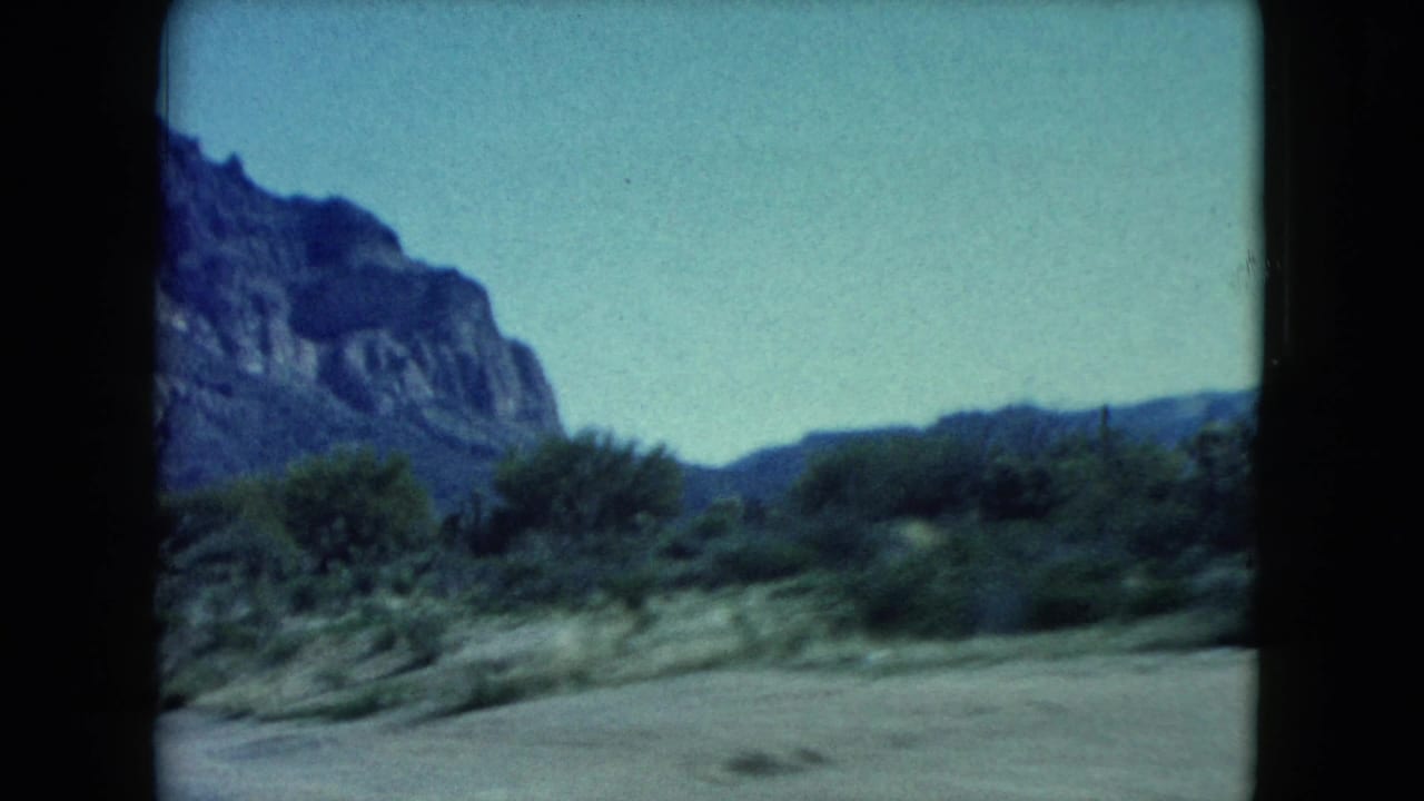 1960 Nevada desert scenery appears through the car interior, with mountains, brush, pale sky, and roadside ground in soft focus.