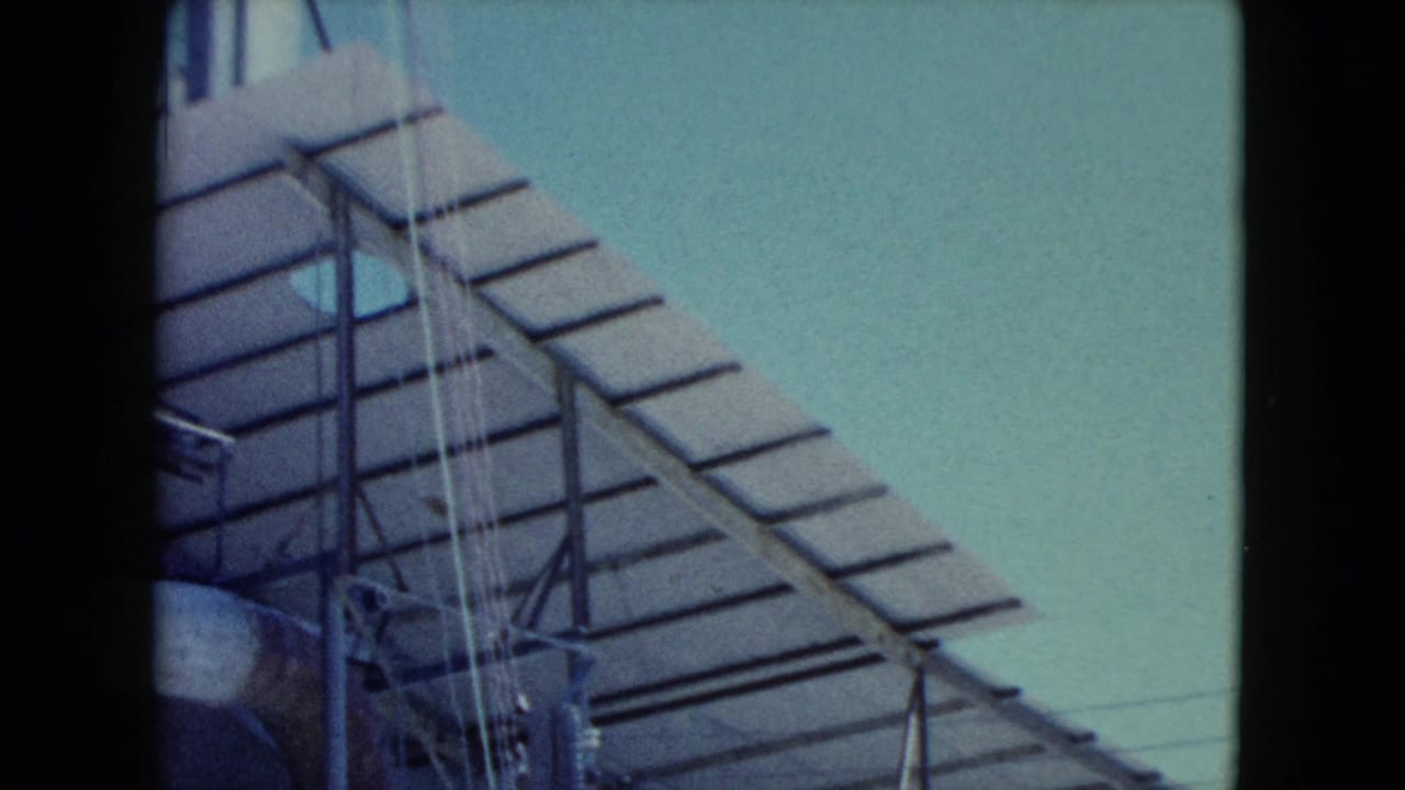 1960 Nevada 8mm frame focused on slatted metal roofing, vertical supports, cables, and a partial pipe at an industrial site.