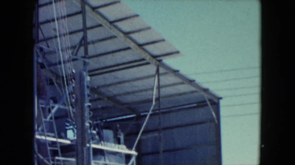 1960 Nevada 8mm frame showing a corrugated metal structure, roof framing, power lines, and dark film borders.