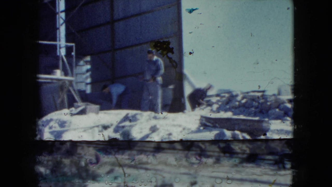 1960 Nevada frame with two workers at a rubble-strewn industrial site, one standing and one bent over near a large doorway.