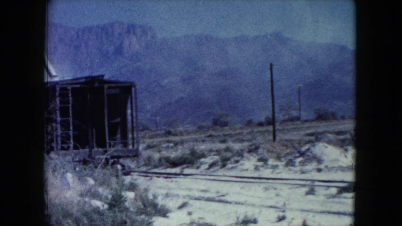1960 Nevada 8mm frame showing an aging rail car near tracks, desert scrub, utility poles, and distant mountains.
