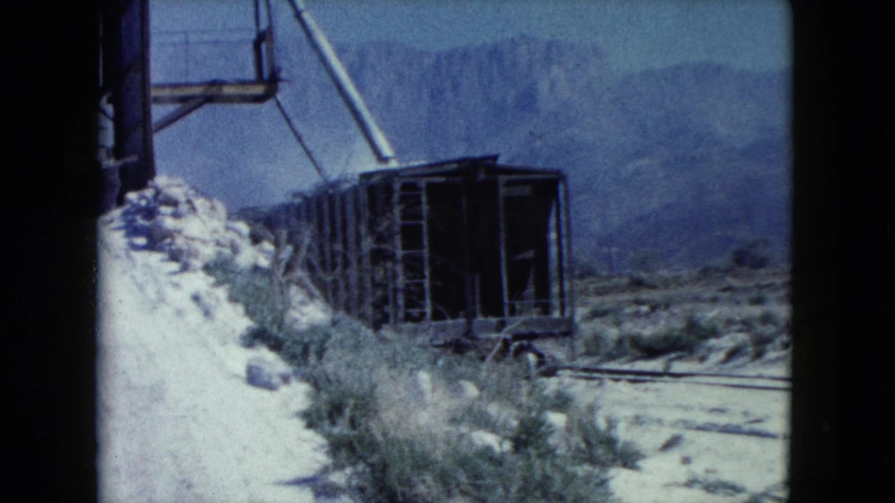 Open industrial rail cart beside a pale dirt road in desert terrain with mountains behind.