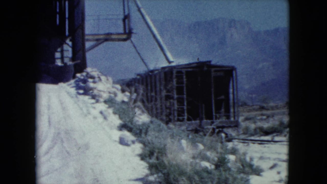 Weathered rail cart and industrial structure along a desert road with mountains in the distance.
