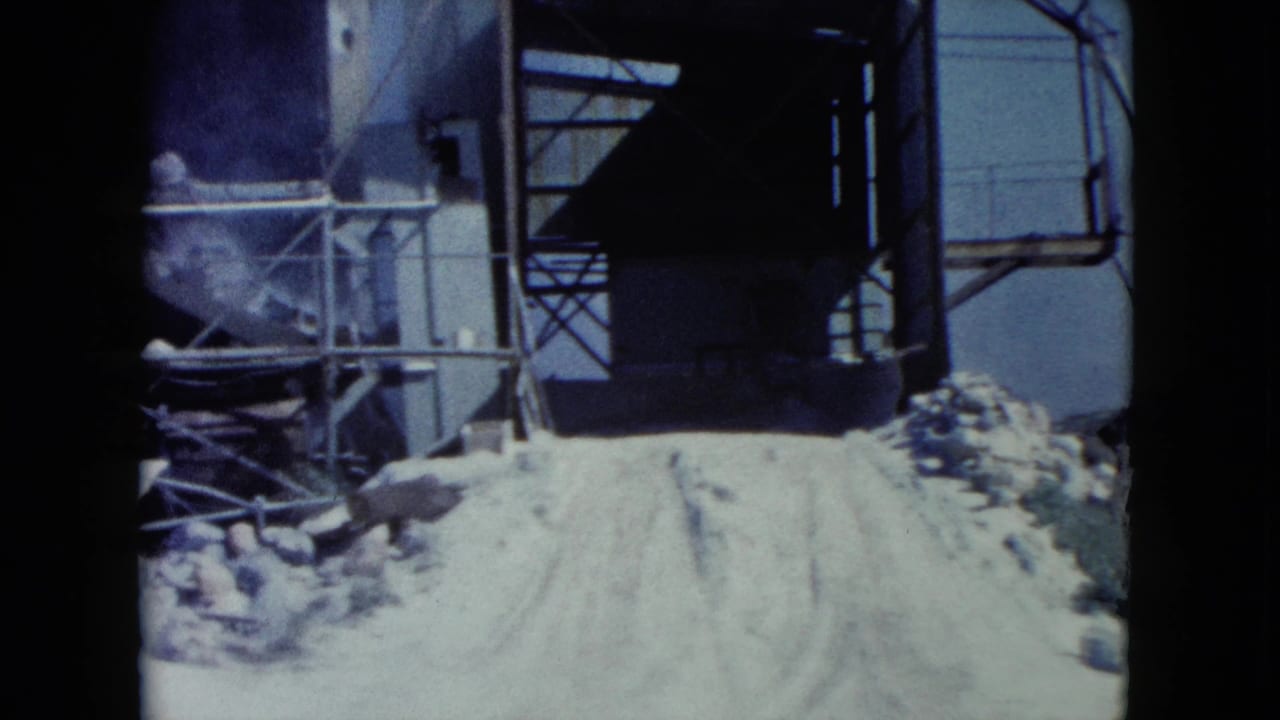 1960 Nevada frame showing metal processing or loading equipment beside a pale road in rocky desert terrain.