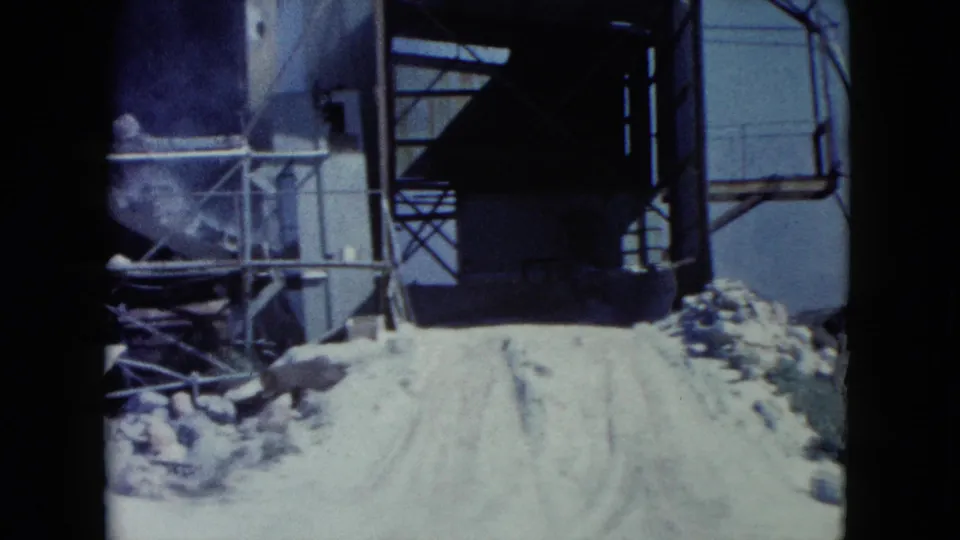 1960 Nevada frame showing metal processing or loading equipment beside a pale road in rocky desert terrain.