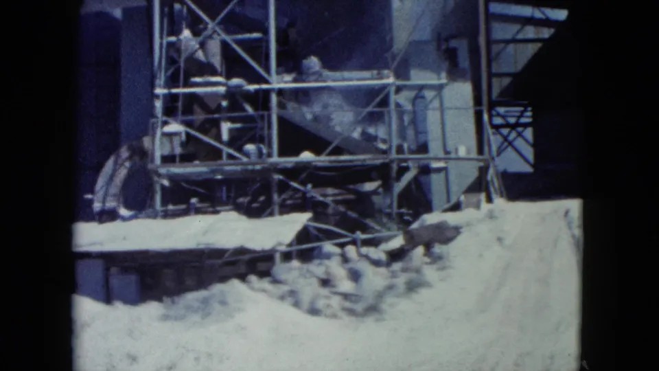 1960 Nevada construction view with metal scaffold work, a tall industrial structure, and pale sand piles in front.