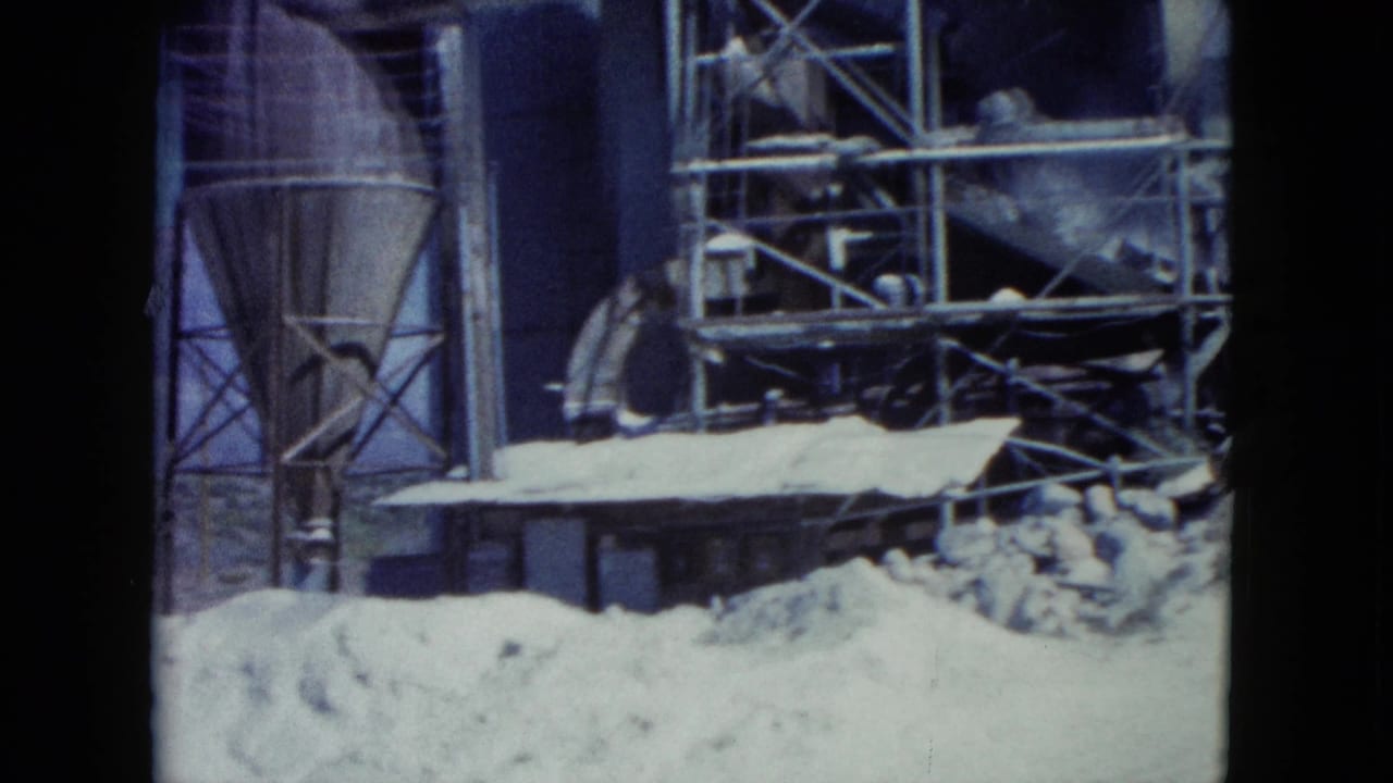 1960 Nevada 8mm frame showing a silo-like structure, scaffold sections, a low building, and sand piles.