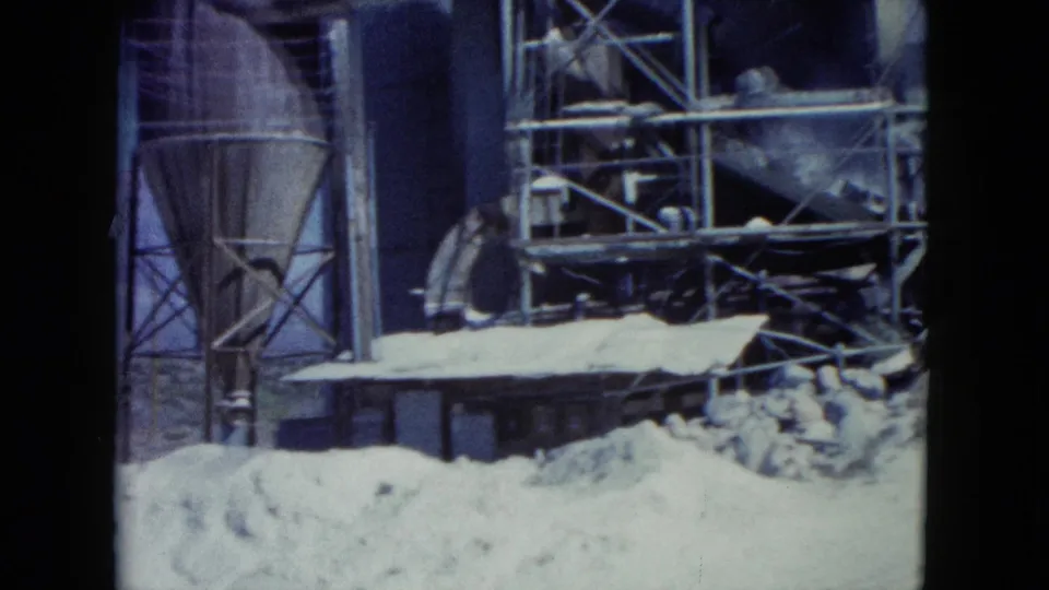 1960 Nevada 8mm frame showing a silo-like structure, scaffold sections, a low building, and sand piles.