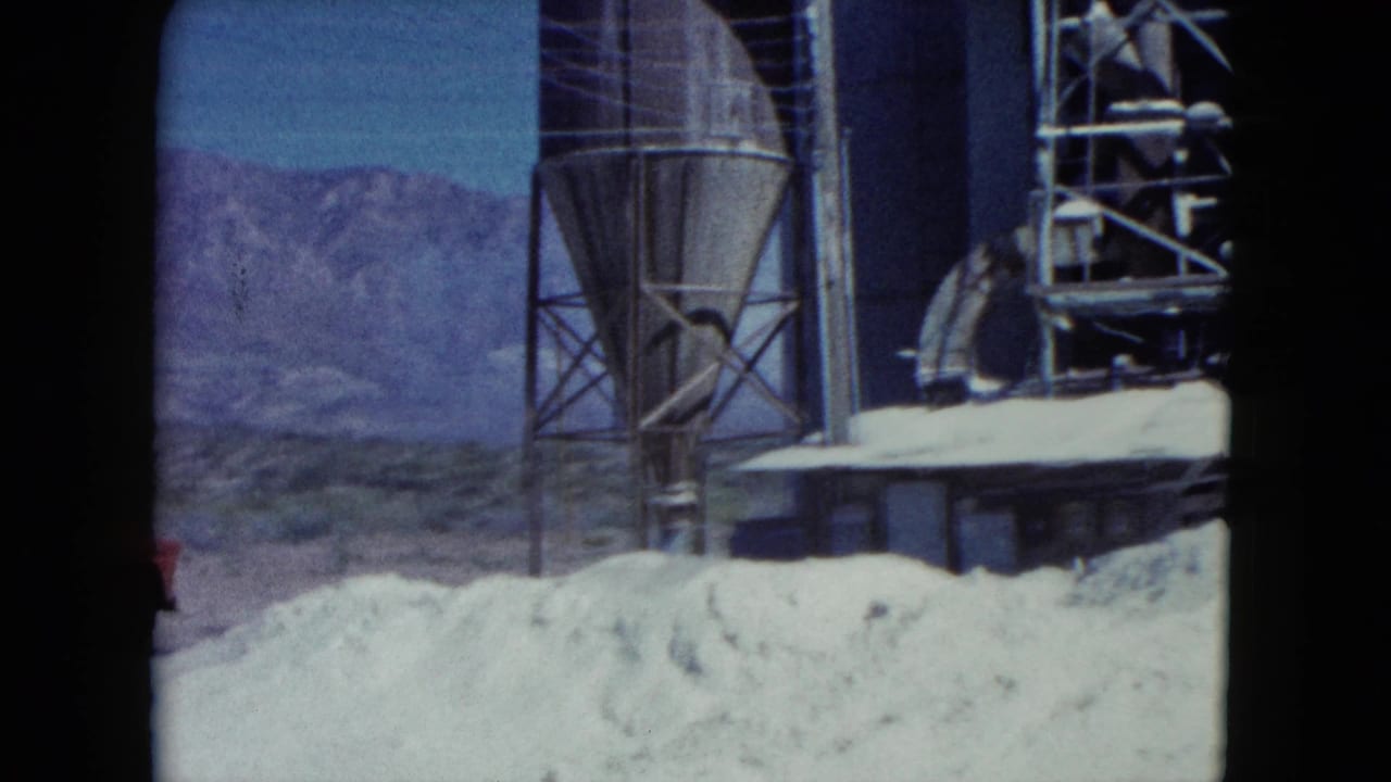 1960 Nevada construction frame with a silo-like structure, scaffolding, sand piles, and mountains in the background.