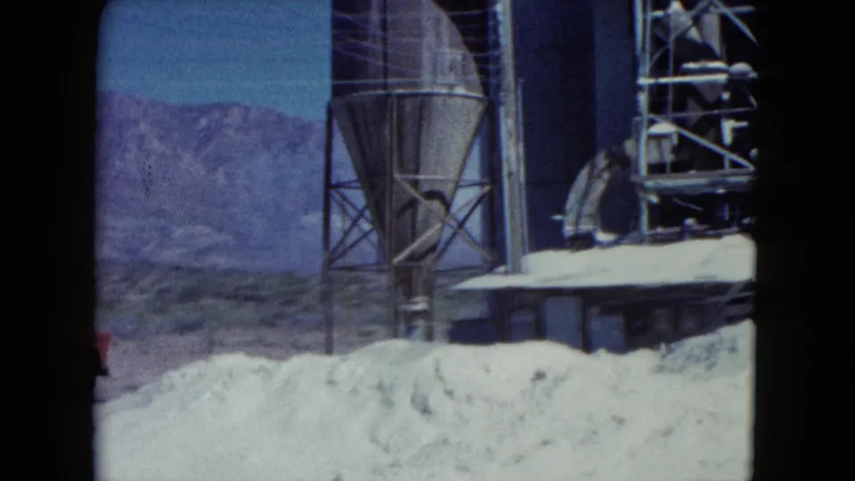1960 Nevada construction frame with a silo-like structure, scaffolding, sand piles, and mountains in the background.