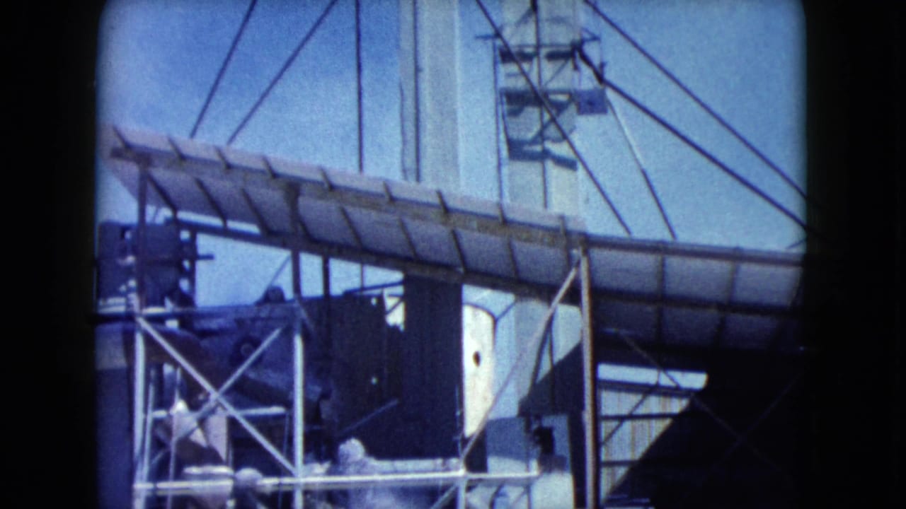 1960 Nevada 8mm frame showing a long elevated conveyor, metal supports, cables, and a pale industrial building under clear sky.