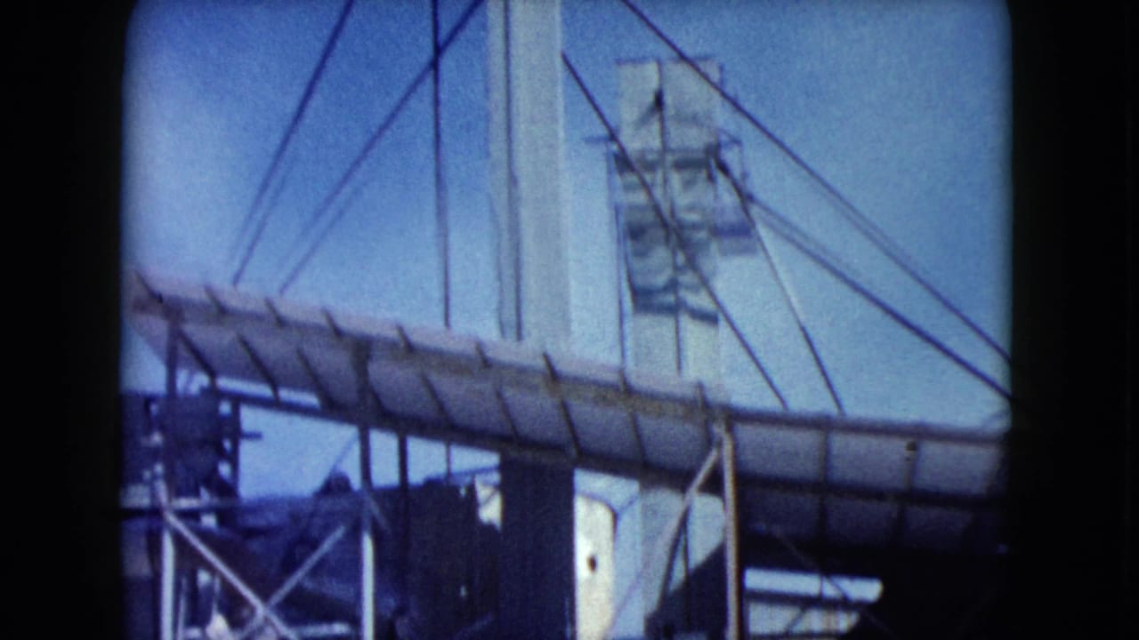 1960 Nevada 8mm frame showing a white industrial tower, cable supports, and a covered conveyor beneath a clear blue sky.