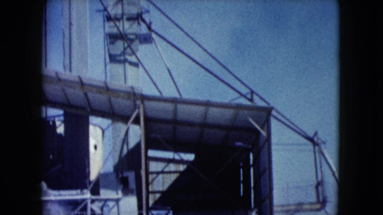 1960 Nevada 8mm frame showing a covered conveyor, white tower edge, steel supports, and open sky at the industrial site.
