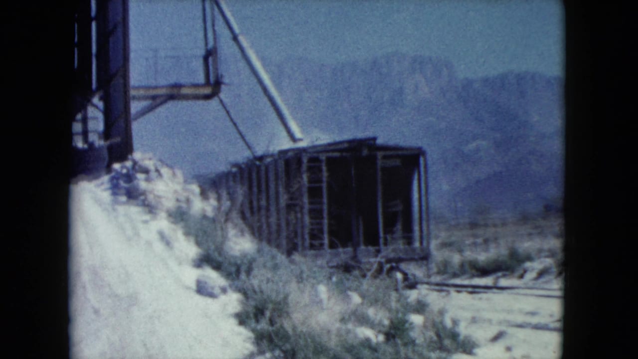 Abandoned metal structure beside pale desert slope and scrub.