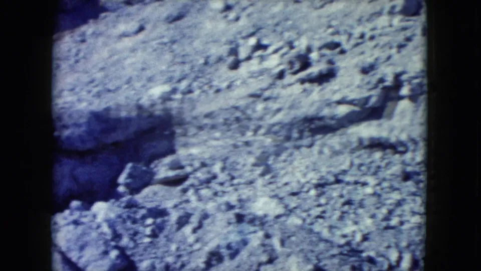 1960 Nevada frame showing a gravelly desert slope, scattered rocks, and eroded pale soil in handheld 8mm color.
