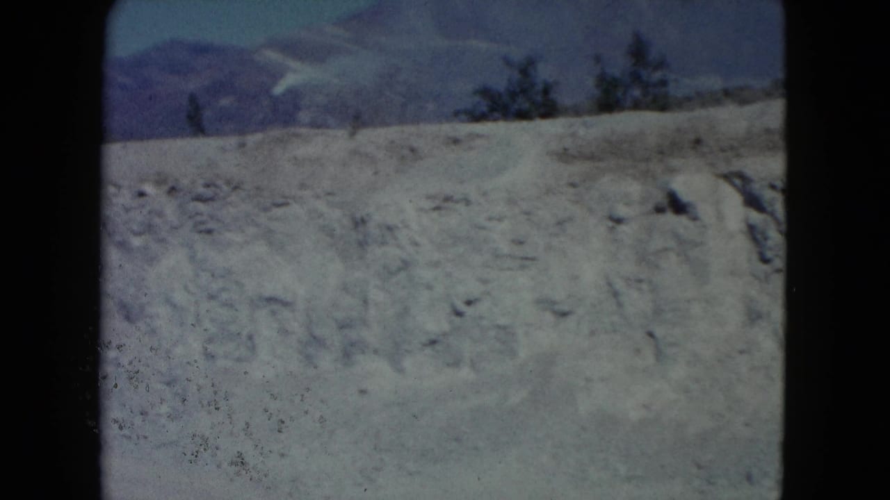 1960 Nevada home-movie still of a dry hillside under blue sky, with mountains beyond and visible 8mm gate edges.