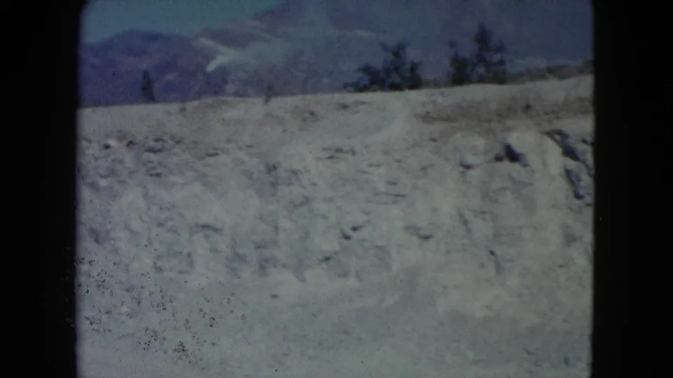 1960 Nevada home-movie still of a dry hillside under blue sky, with mountains beyond and visible 8mm gate edges.