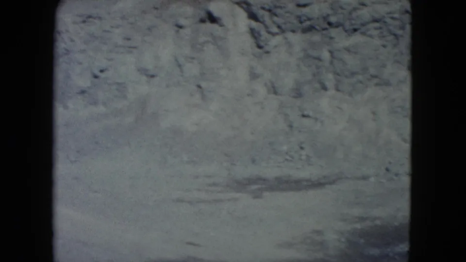 1960 Nevada 8mm frame focused on an eroded dirt bank and rocky ground, with the horizon mostly out of view.