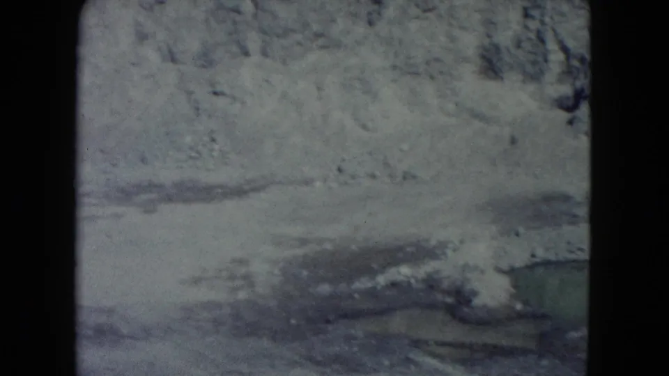 1960 Nevada 8mm still showing a rocky pale hillside and sparse scrub, softened by grain and faded color.
