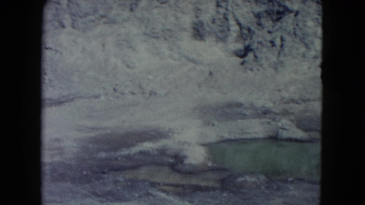 Snow-dusted rocky ground with a small greenish water pool and dark film borders.