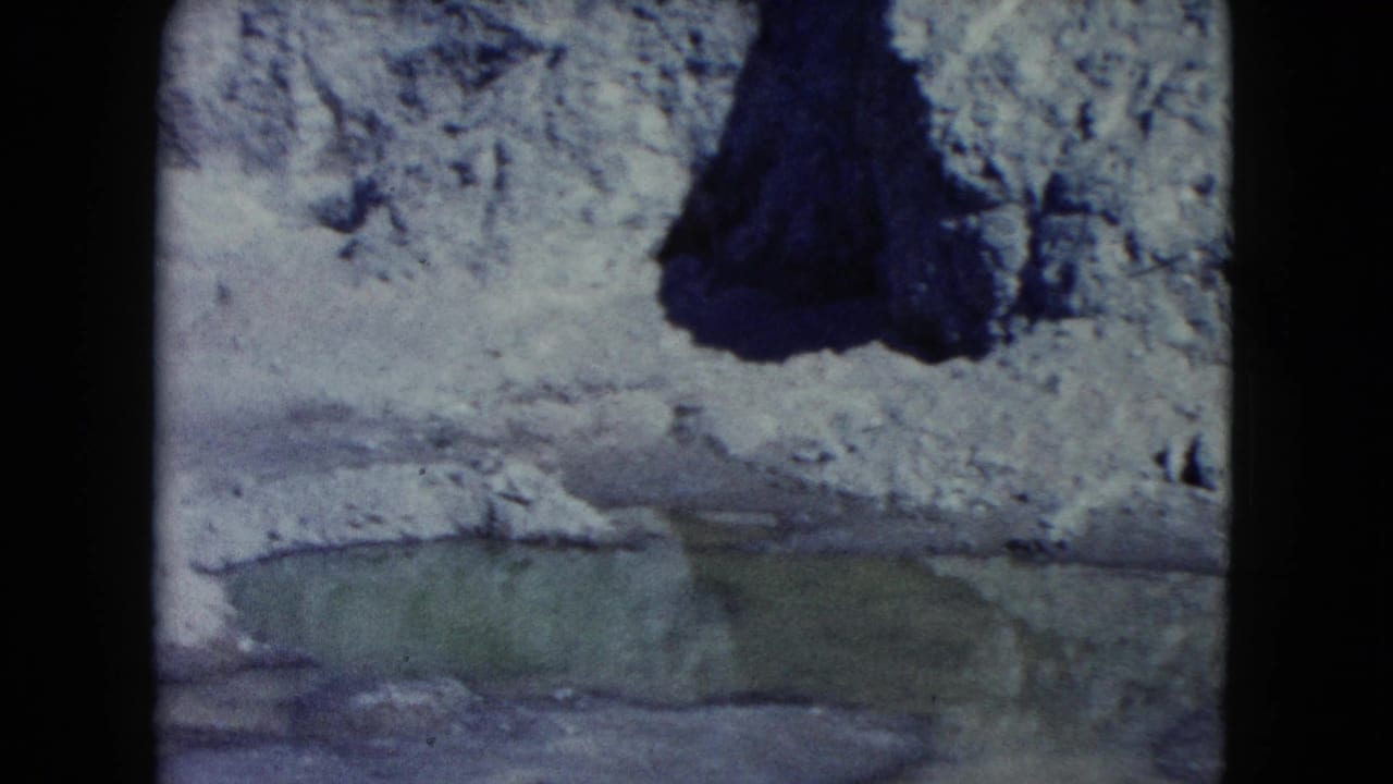 1960 Nevada 8mm frame showing icy rock, a greenish foreground pool, and a dark cave-like opening in the upper right.