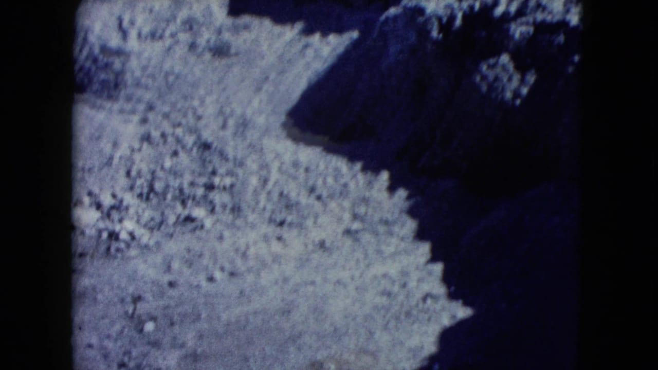 1960 Nevada 8mm frame of rough desert rock and eroded ground, rendered with blue color shift, grain, and heavy shadow.