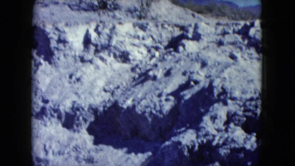 1960 Nevada 8mm frame looking across uneven rocky desert terrain with a dark shadowed hollow in the foreground.