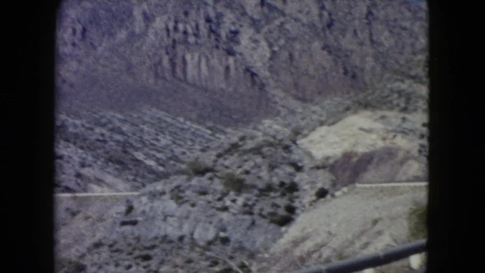 1960 Nevada 8mm frame looking across a rocky arid valley, with a road edge and guardrail in the foreground.
