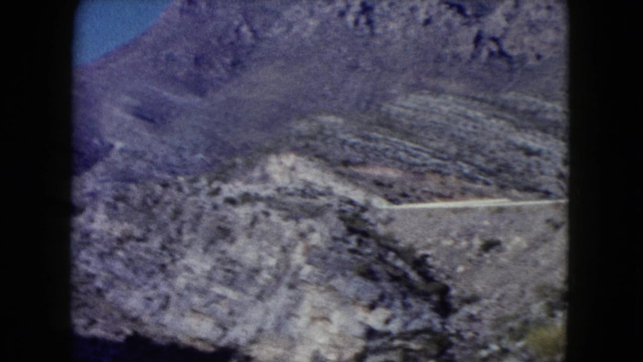 Distant 1960 Nevada travel view of a winding road on barren mountain terrain, seen through soft 8mm film grain.