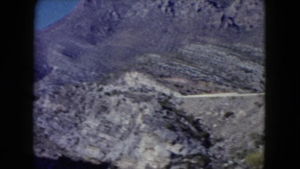 Distant 1960 Nevada travel view of a winding road on barren mountain terrain, seen through soft 8mm film grain.