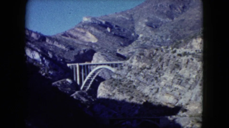 1960 Nevada home-movie frame showing a concrete arch bridge across a rocky canyon in arid mountain terrain.