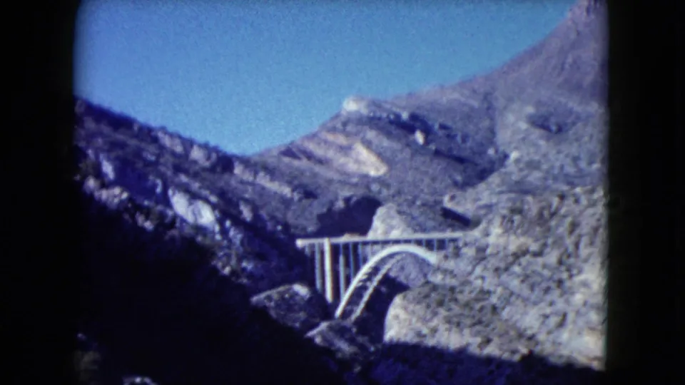Soft 8mm view of a concrete arch bridge in Nevada mountain country, framed by canyon shadow and bright blue sky.