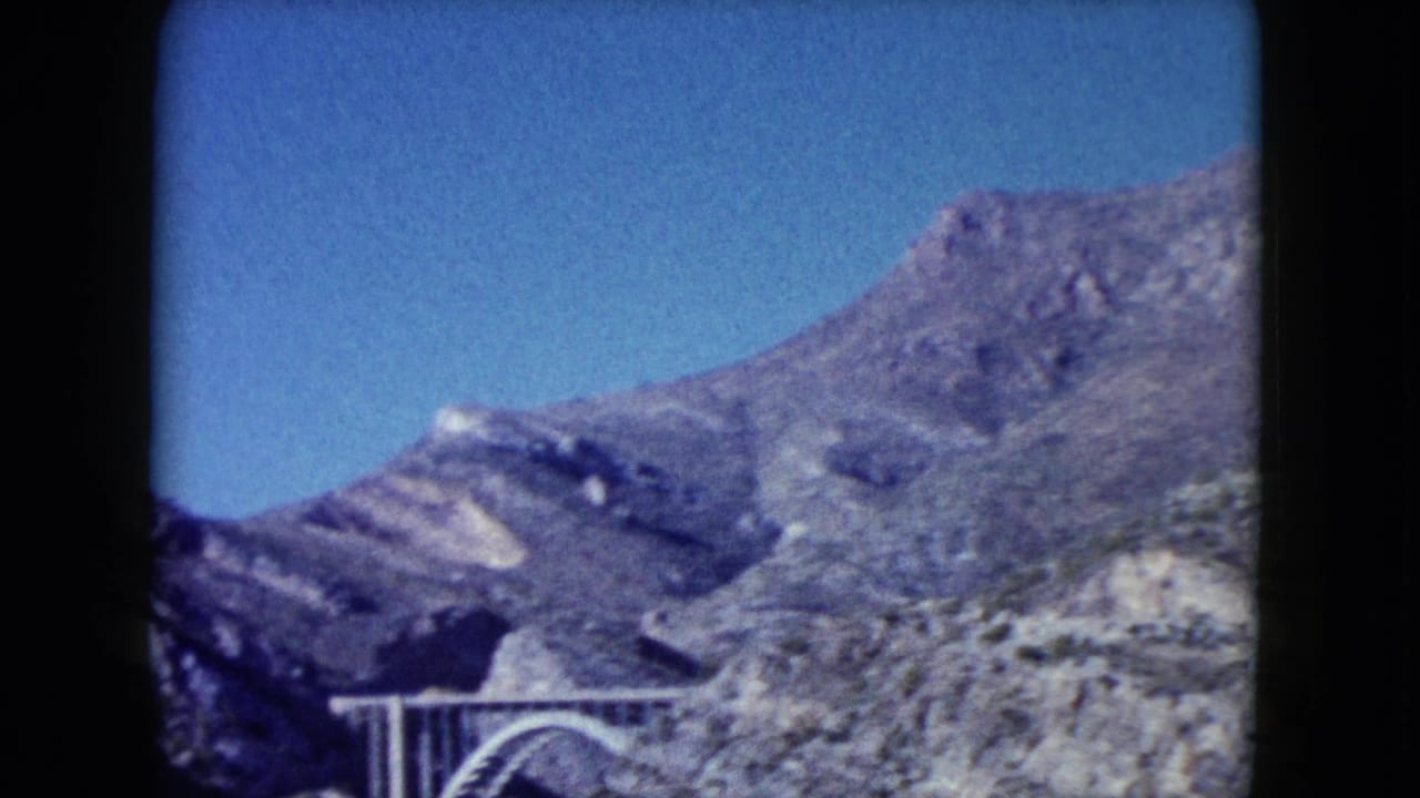 1960 Nevada 8mm frame showing rugged hills and a partial arched bridge against a clear blue sky.