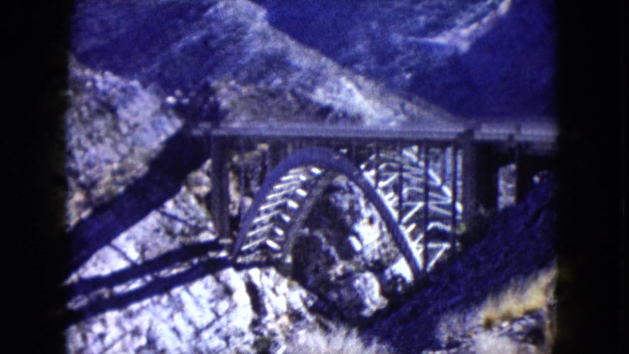 1960 Nevada 8mm frame showing a steel arch bridge set against steep rocky canyon terrain.