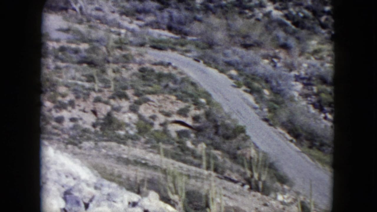 Rocky desert hillside with an empty winding road and sparse scrub.