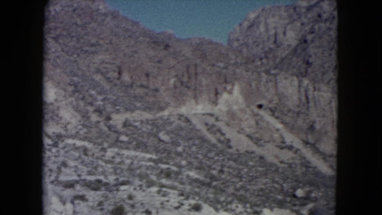 1960 Nevada home-movie view of rugged desert mountains and pale rocky slopes under blue sky, framed by dark film edges.