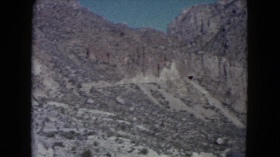 1960 Nevada home-movie view of rugged desert mountains and pale rocky slopes under blue sky, framed by dark film edges.