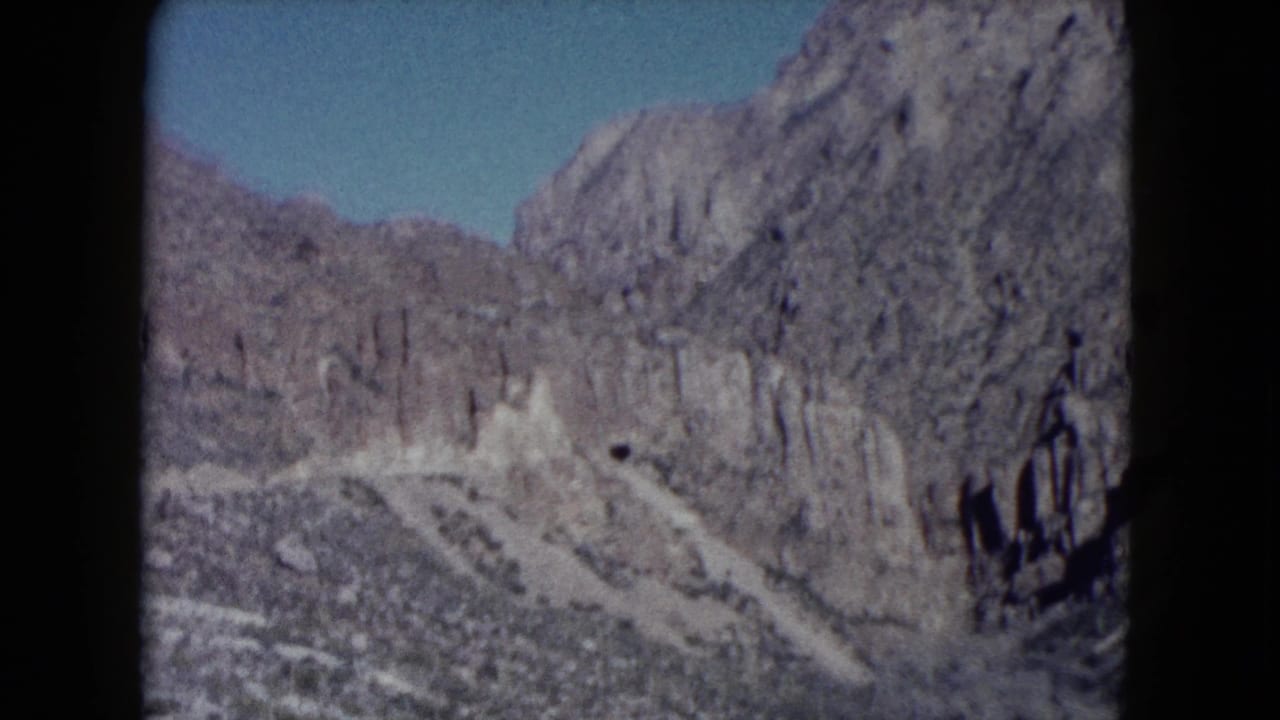 1960 Nevada 8mm travel frame showing steep rocky canyon walls, pale desert wash, and blue sky through soft film grain.