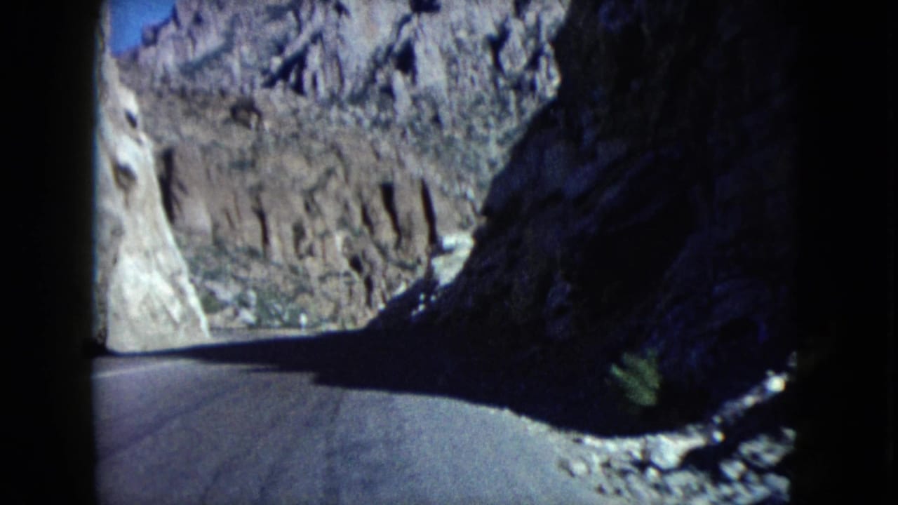 1960 Nevada 8mm road-trip frame showing a paved curve through rocky desert mountains from a moving car perspective.