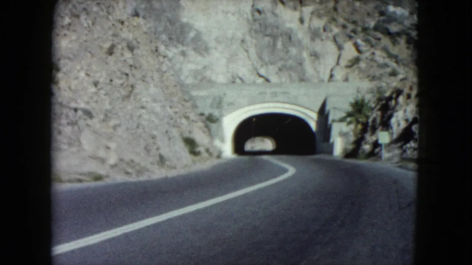 The 8mm frame shows a curving Nevada road leading into a mountain tunnel, with desert rock and palms at the side.
